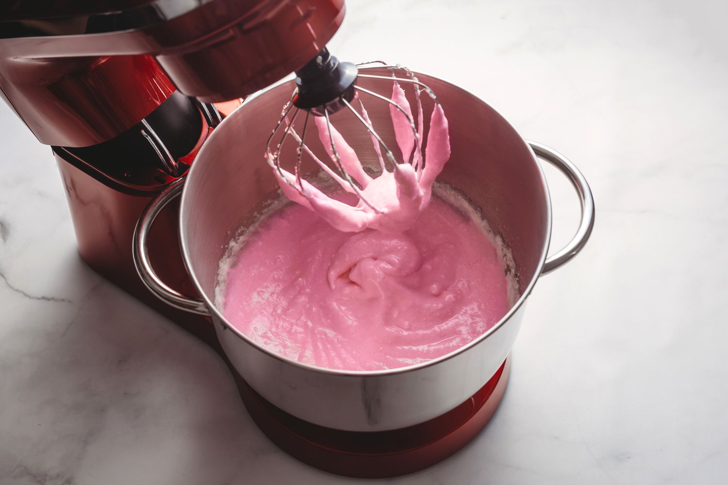 Pink food coloring being incorporated into egg white mixture in the stand mixer