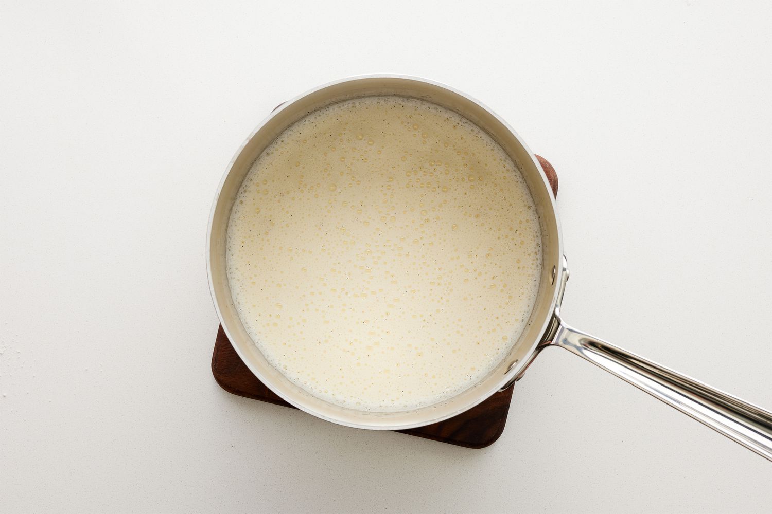 A pot of warmed vanilla, cream and milk, with sugar and salt sitting on a trivet 