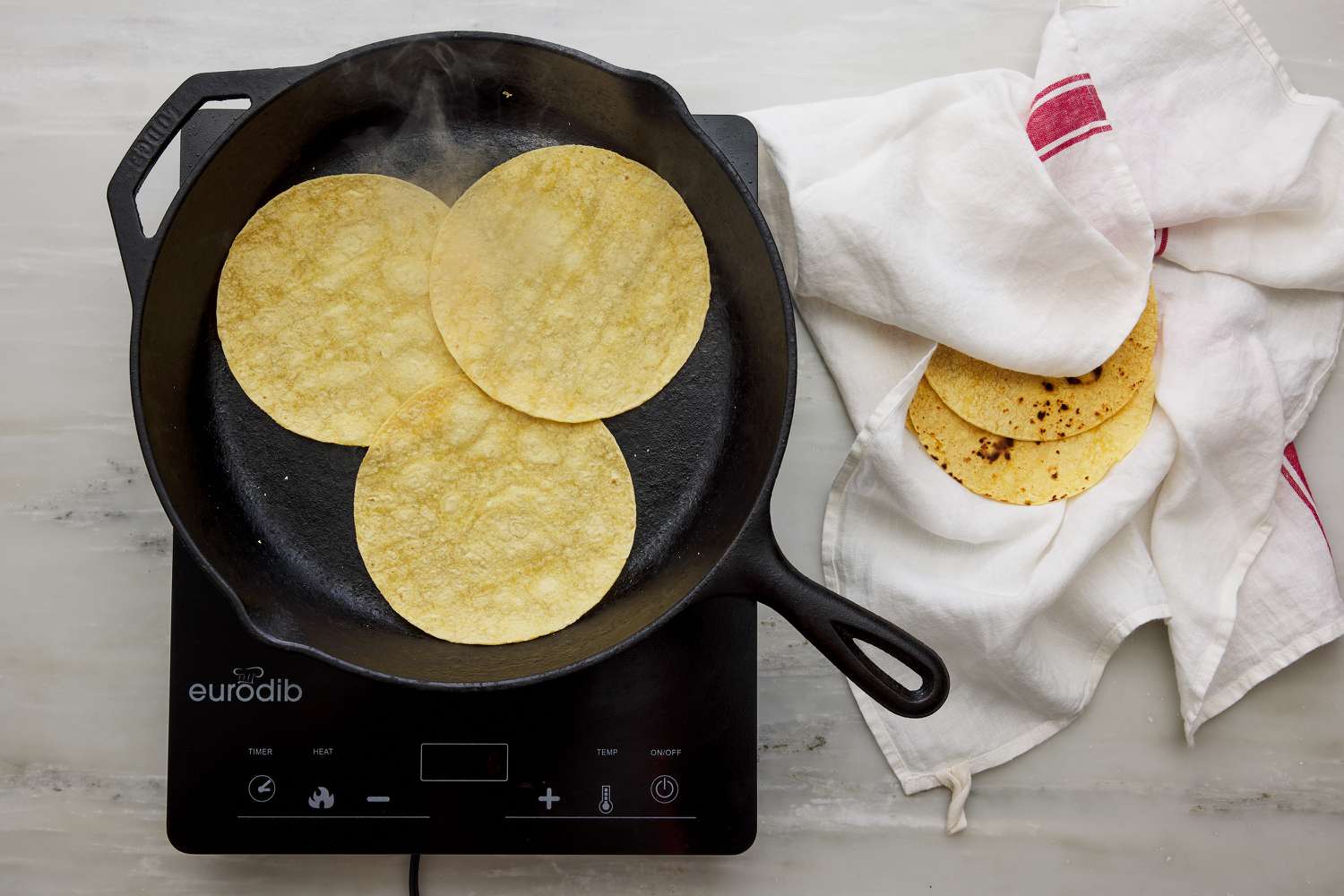 corn tortillas being warmed in large cast iron pan with clean dish towel off to side to keep warm