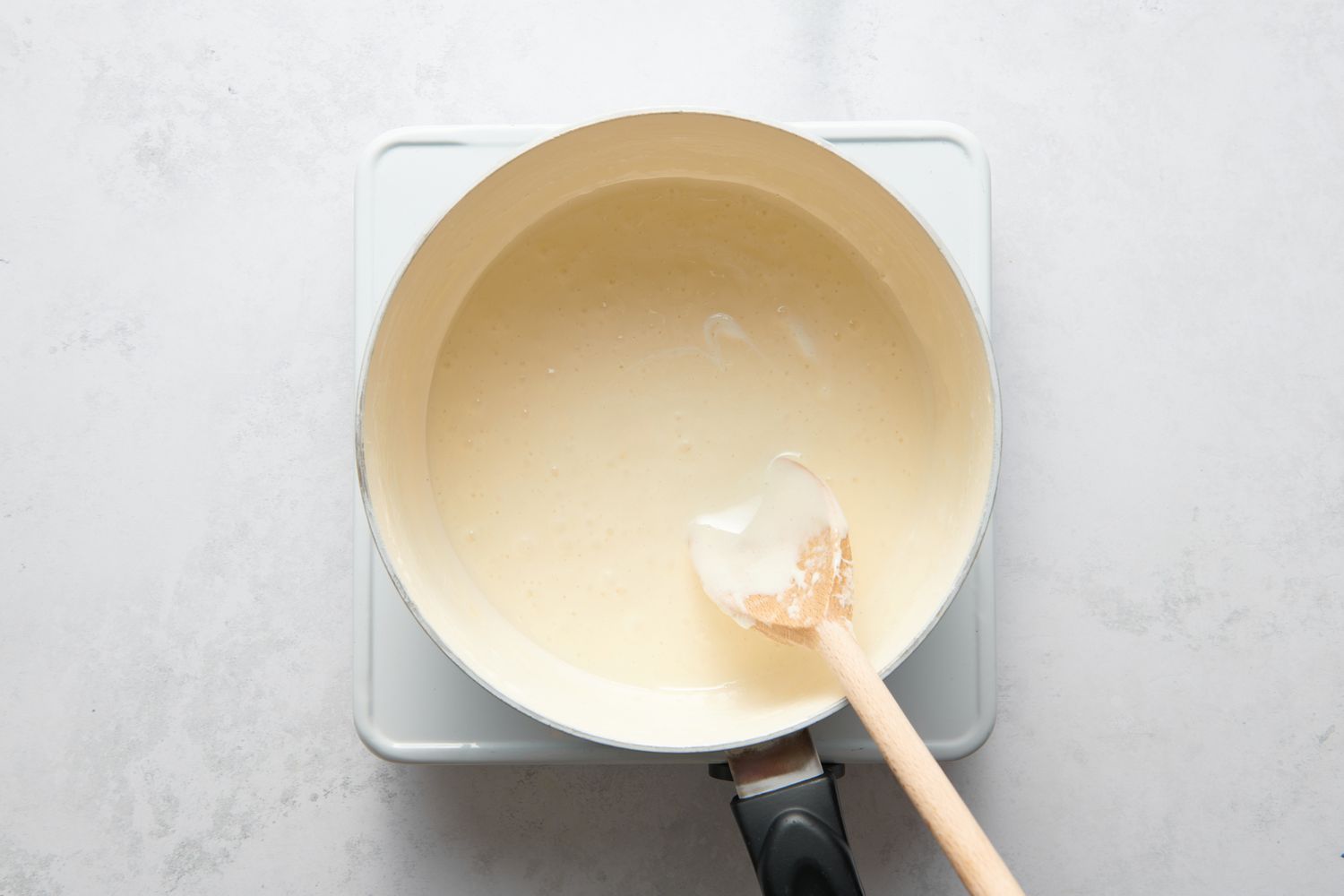 A large pot of melted marshmallows, being stirred with a wood spoon