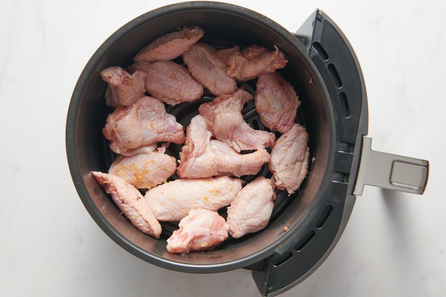 Seasoned chicken wings in an air fryer basket
