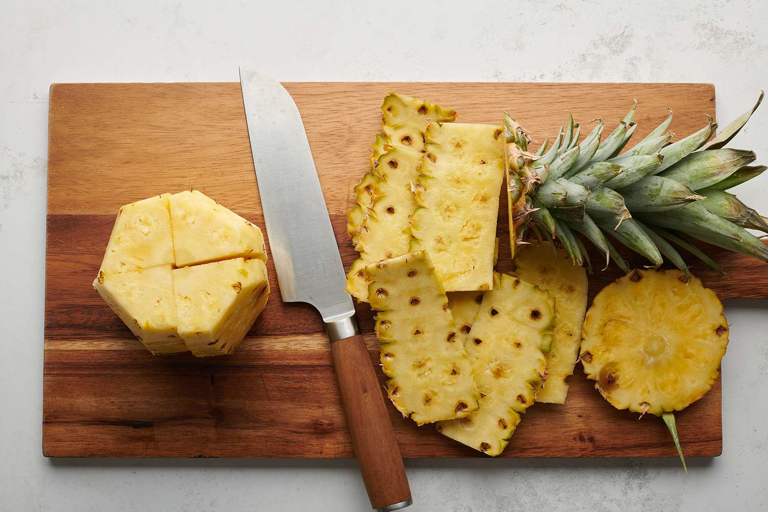 Sliced pineapple with the top and skin removed on a wooden cutting board with a knife