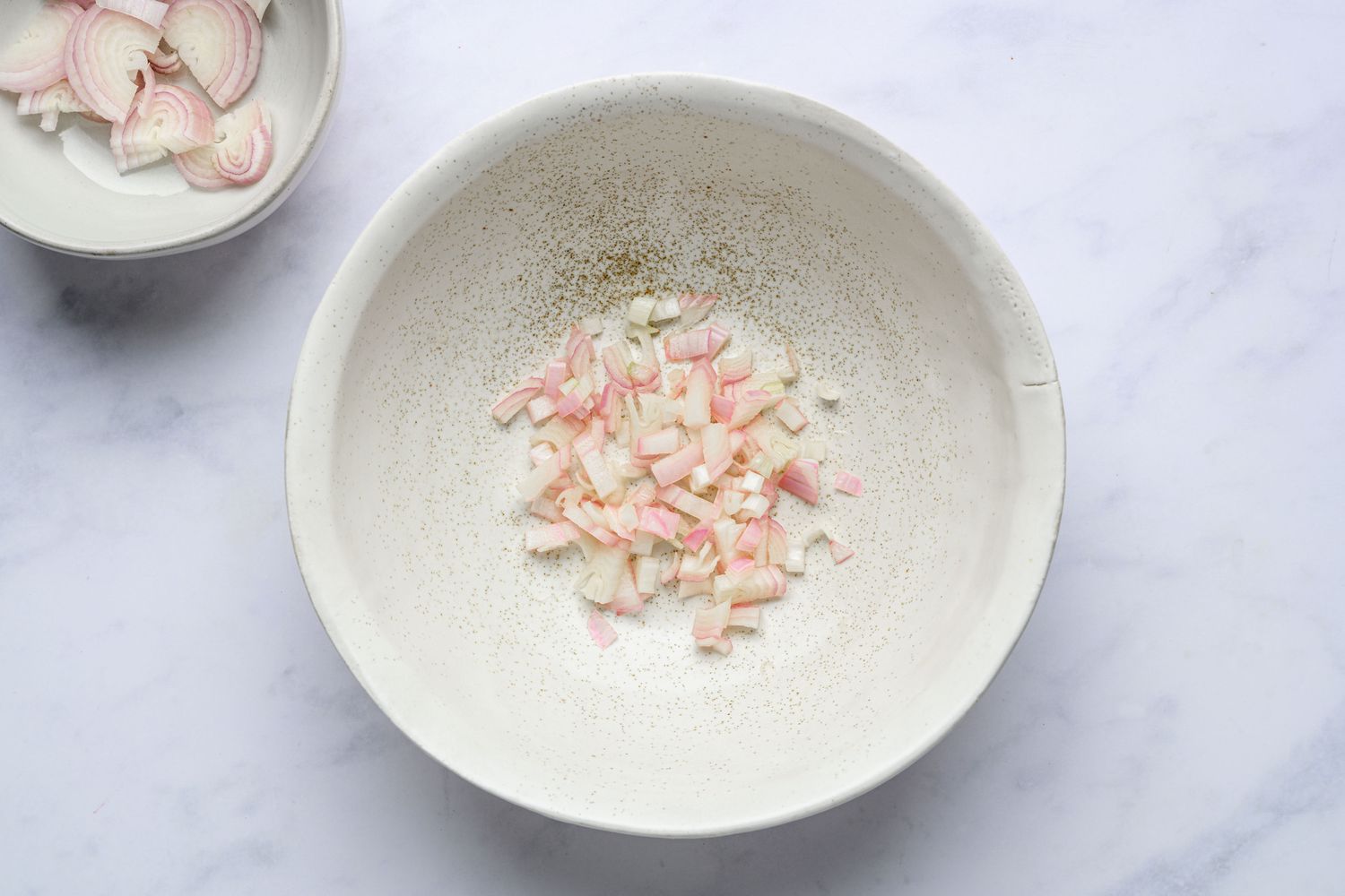 A bowl of thinly shaved shallots and a bowl of diced shallot