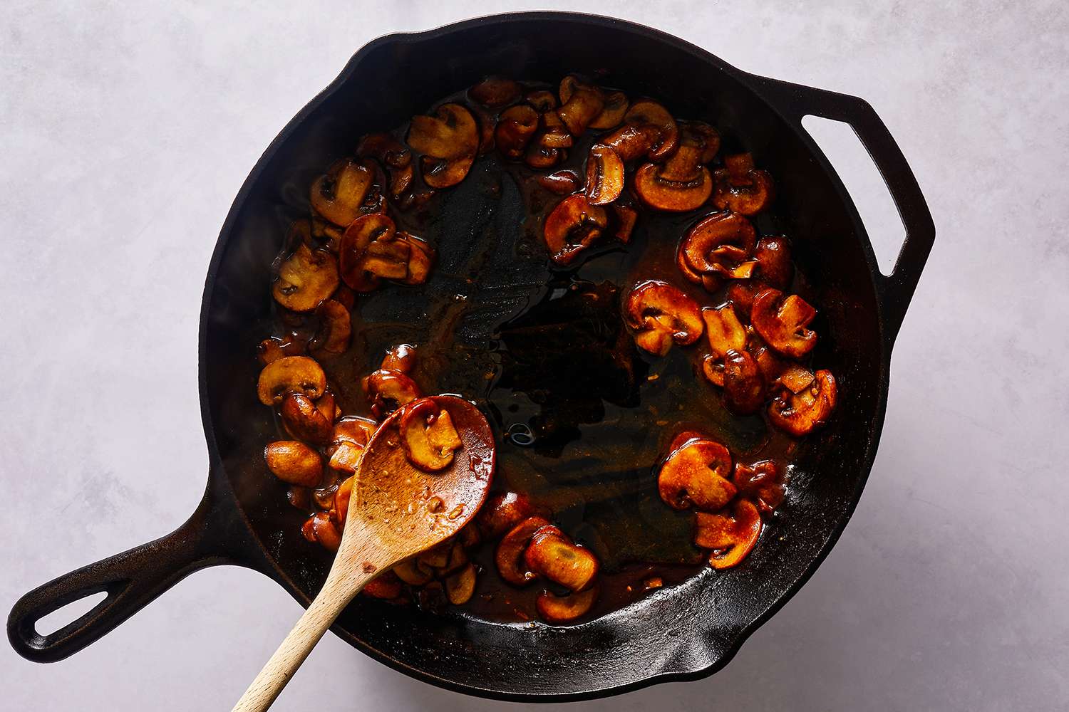 Mushrooms and sauce cooking in a cast iron skillet, with a wooden spoon 