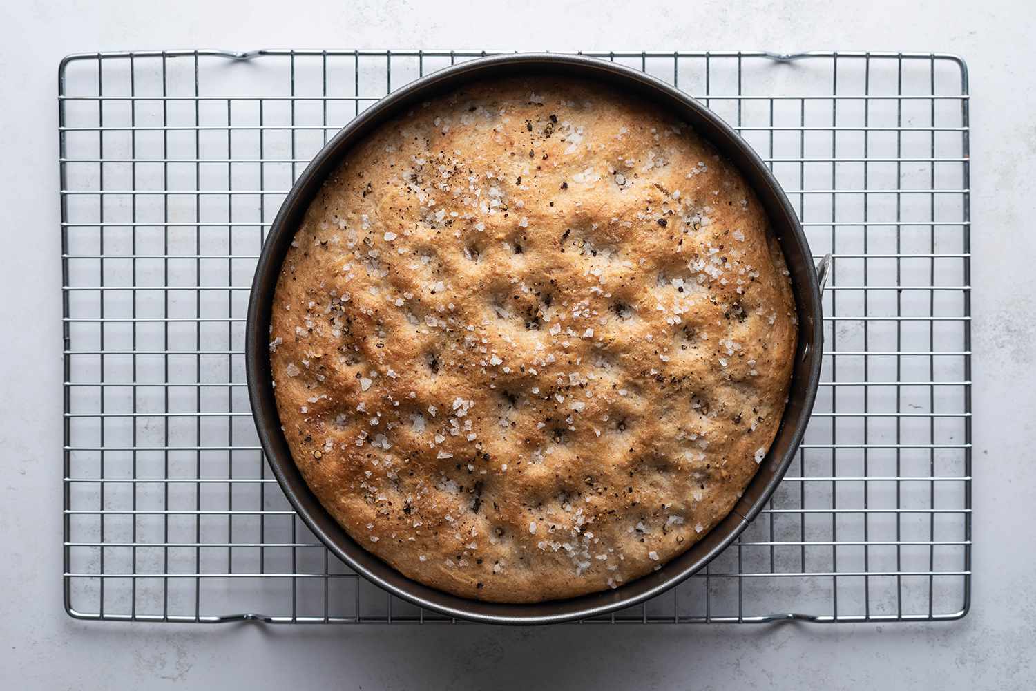 Black Pepper Focaccia in a cake pan on a cooling rack 