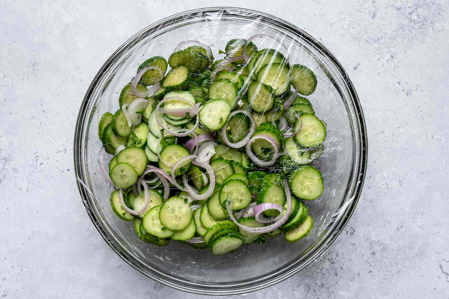 Bowl of cucumber salad covered with plastic wrap