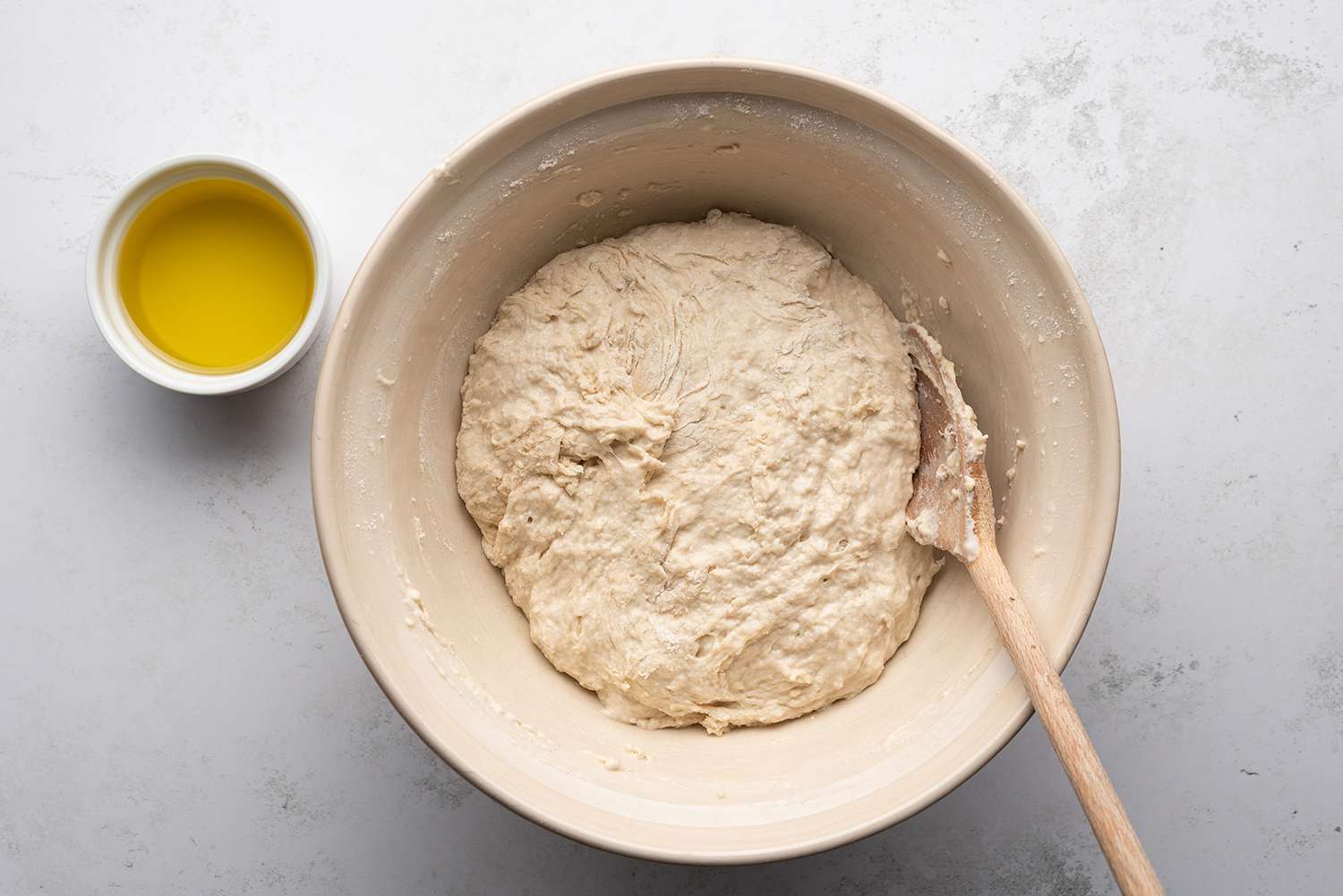 Dough in a bowl with a wooden spoon and oil in a bowl 