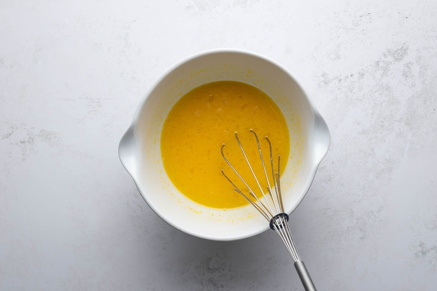 Eggs, yolks, sugar, lemon zest and juice mixture in a bowl with a whisk 