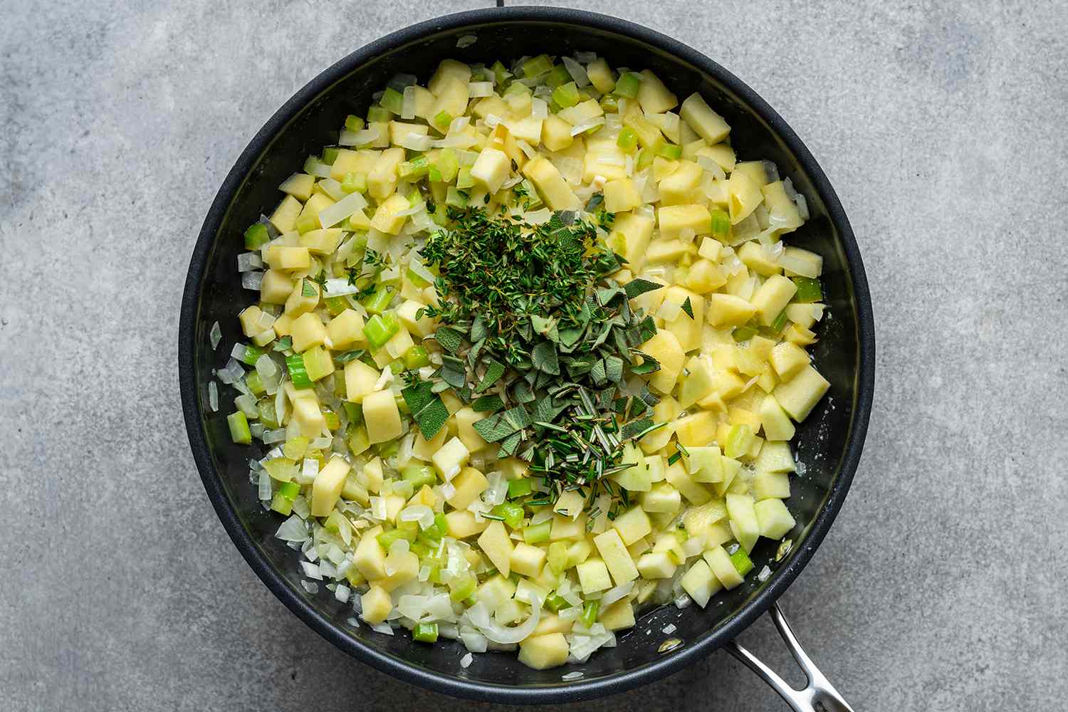 cooked chopped onions, celery and apples with herbs in a skillet