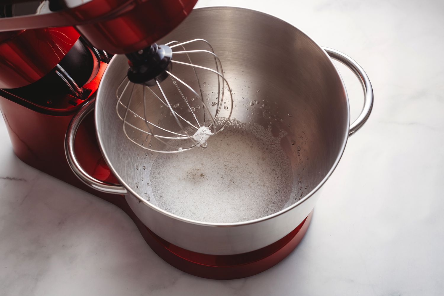 Egg whites in the bowl of the stand mixer with a whisk