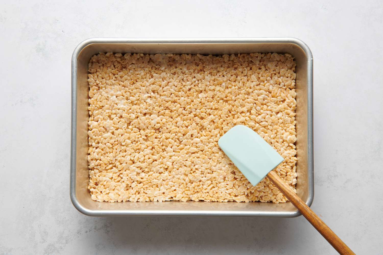 A 9 x 13 baking pan with a layer of puffed rice cereal-marshmallow mixture