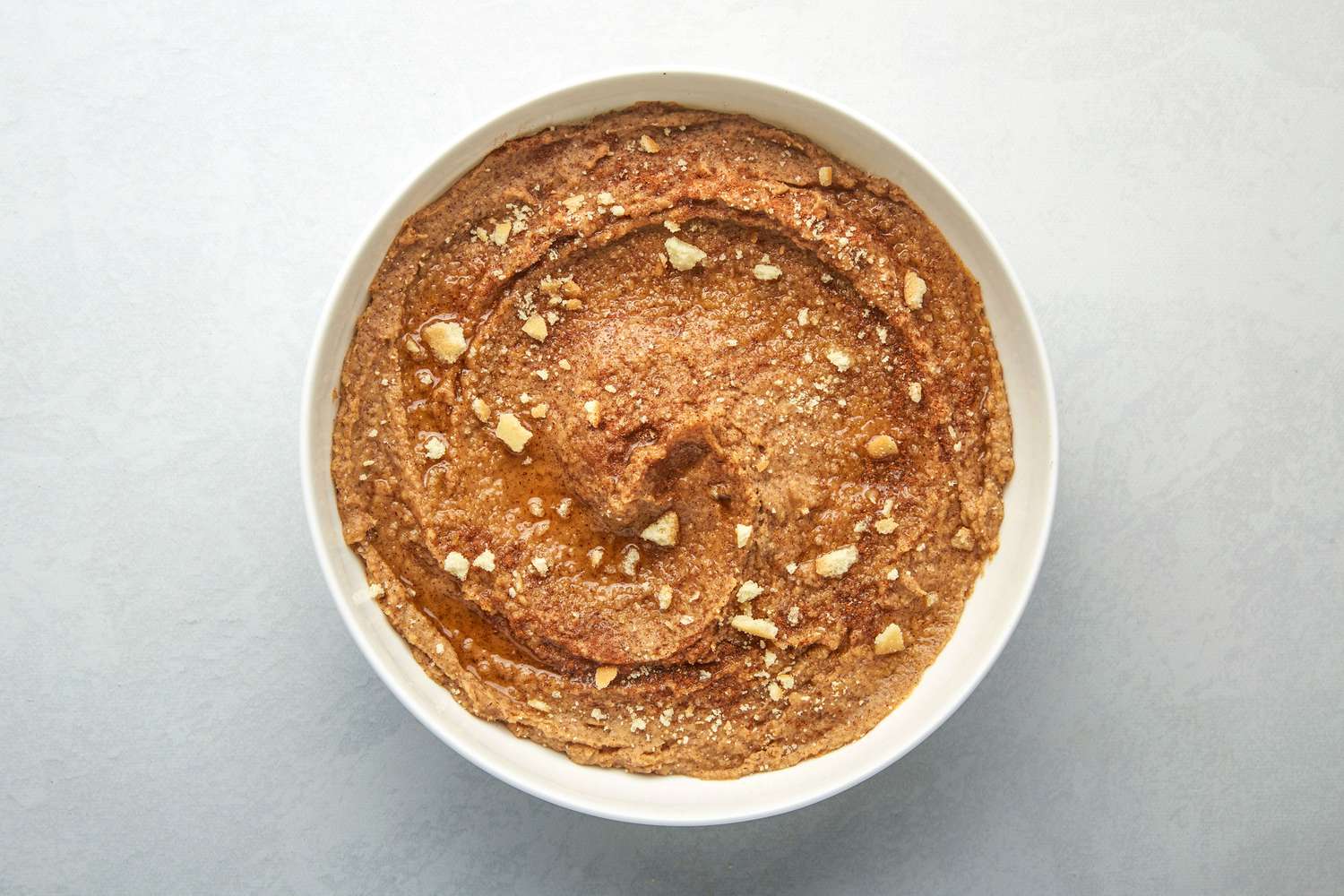 A bowl of snickerdoodle hummus, topped with maple syrup, cinnamon, and crumbled vanilla cookies