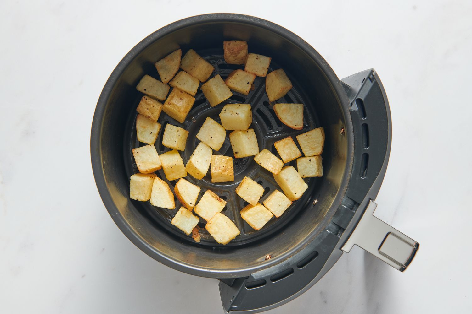An air fryer basket with partially cooked potato chunks