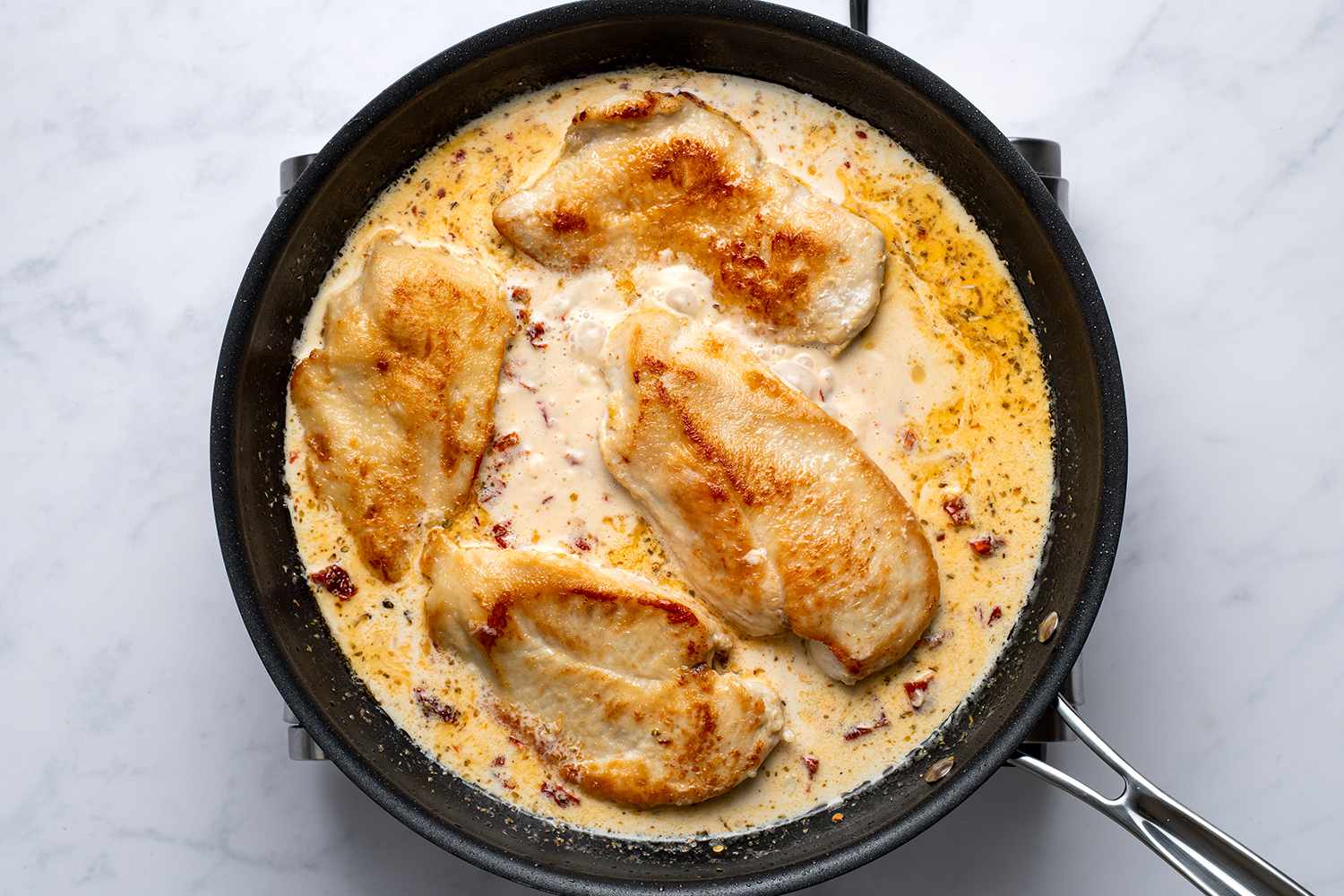Lightly browned chicken breasts in creamy sauce in a skillet