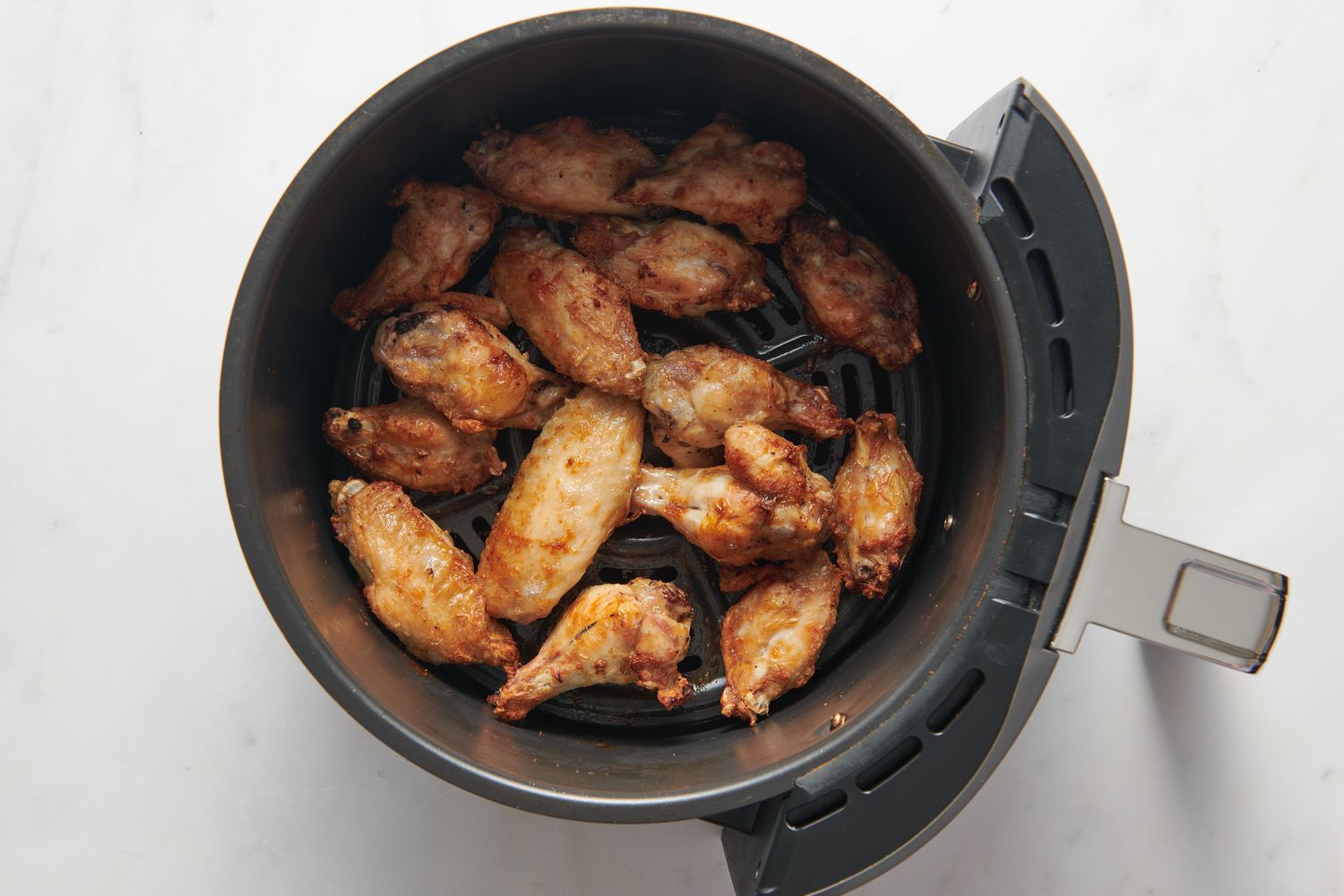 Partially cooked chicken wings in an air fryer basket