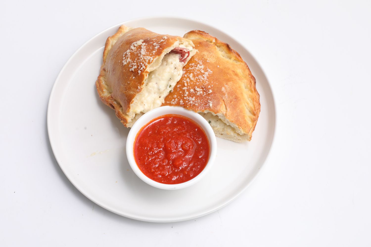 A golden brown calzone cut in half with tomato sauce on the side