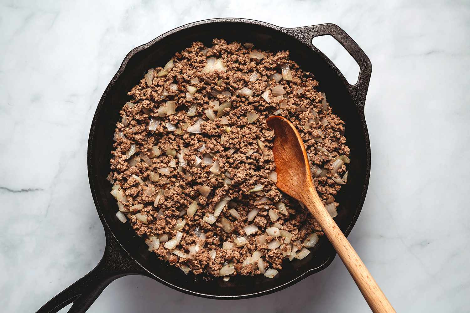 Ground beef and onions in a cast iron pan with a wooden spoon 