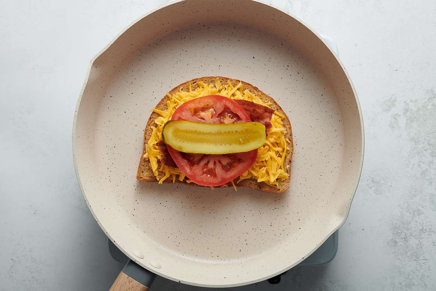 shredded cheese, tomato, bacon and pickle on a slice of bread