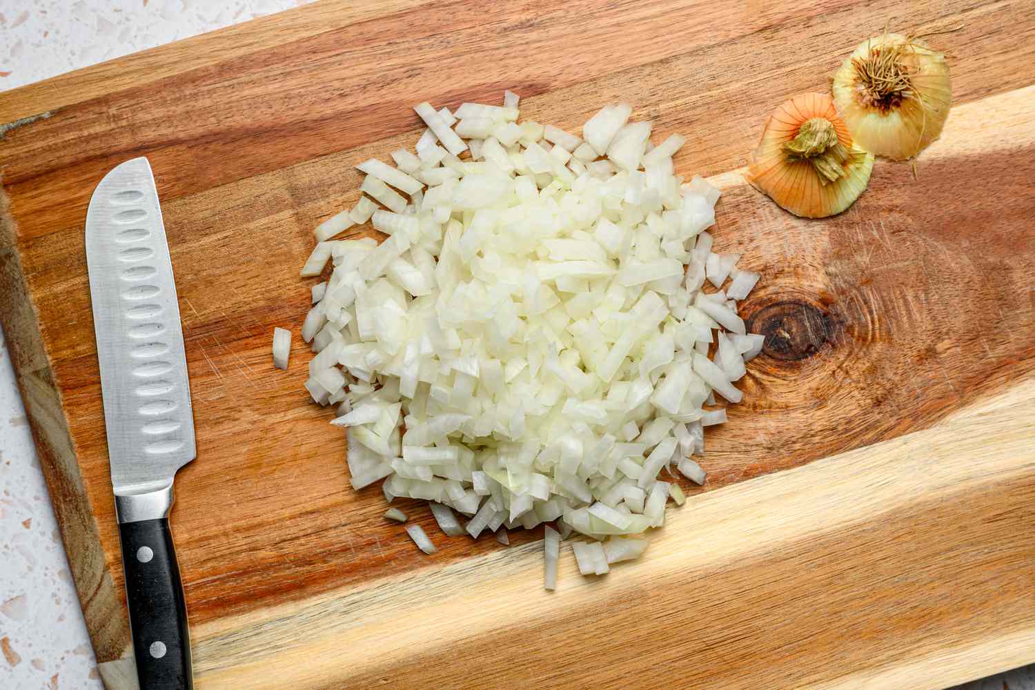 A cutting board with finely diced onion and a knife