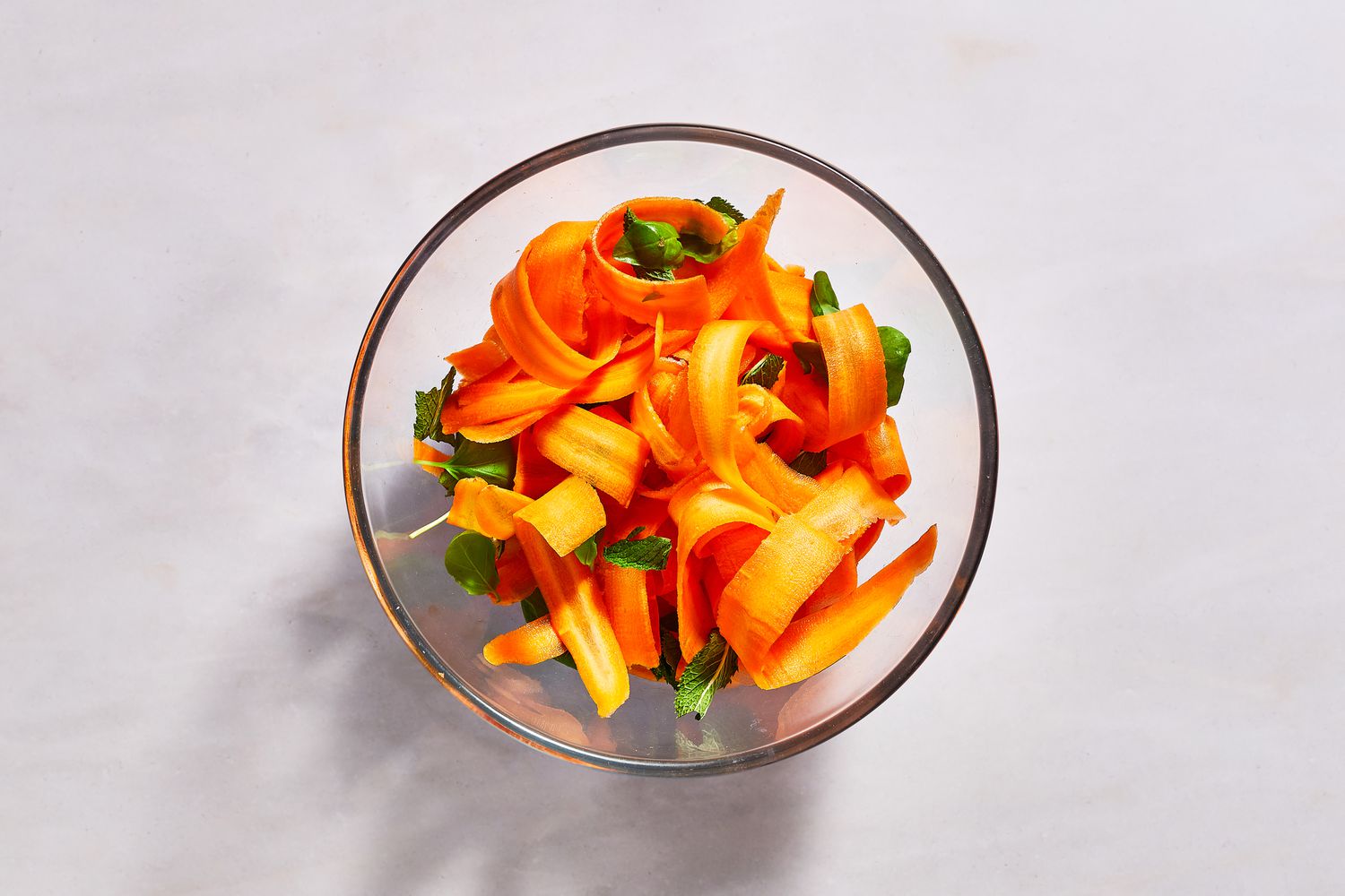 A large bowl of shaved carrot ribbons, mint leaves, and basil leaves