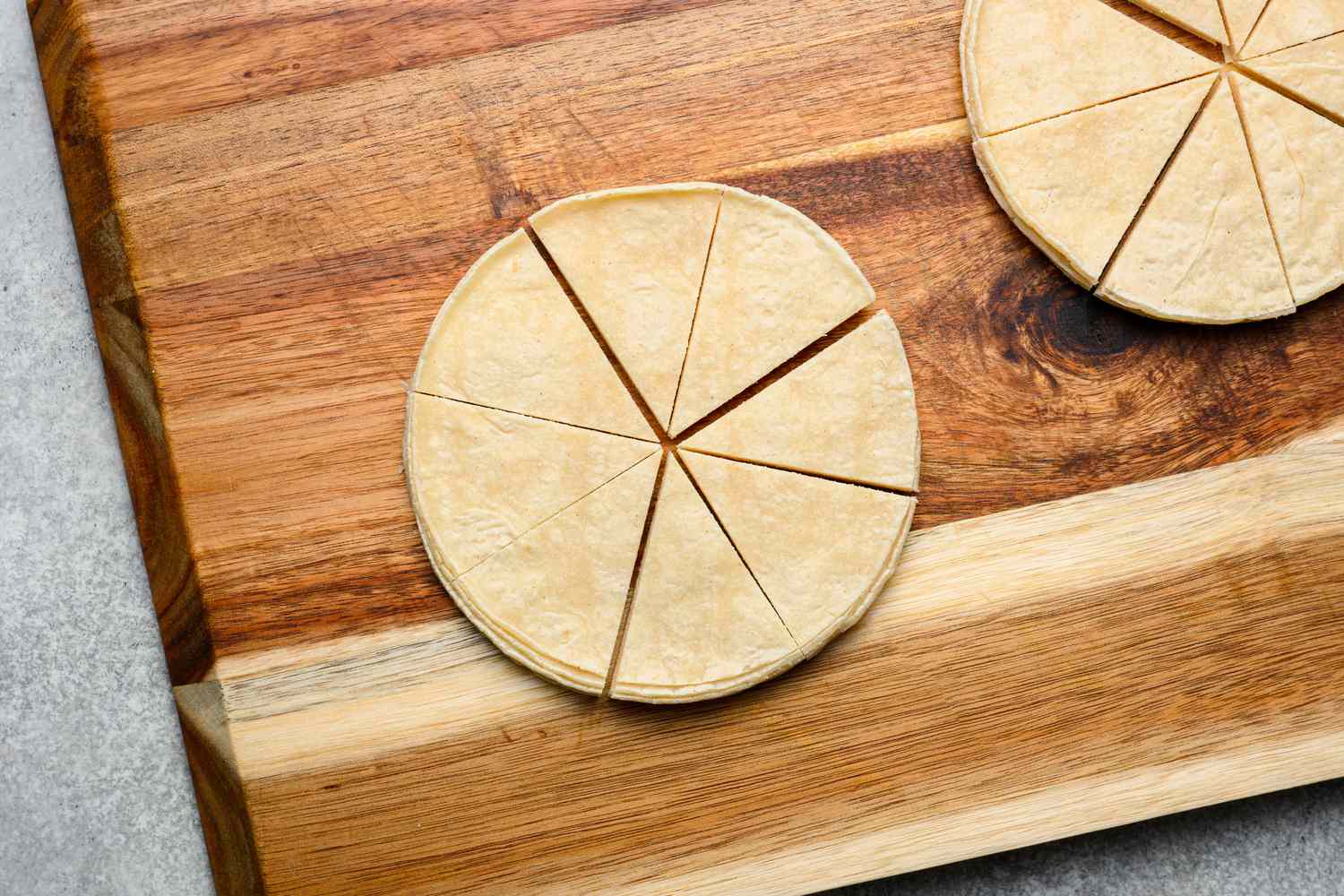A cutting board with a two stacks of corn tortillas cut into eight equal wedges
