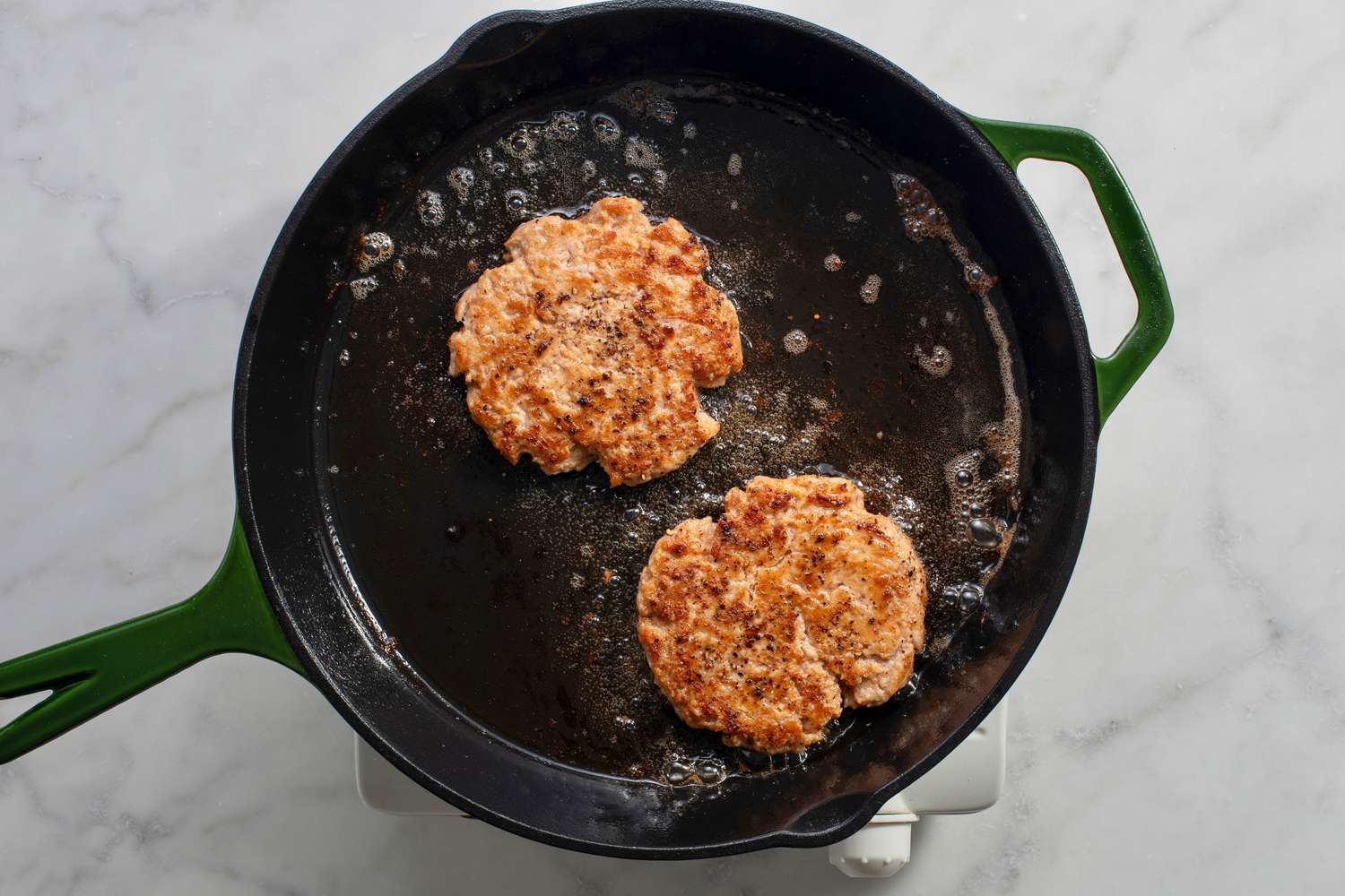 Flipped chicken patties cooking in a cast iron skillet