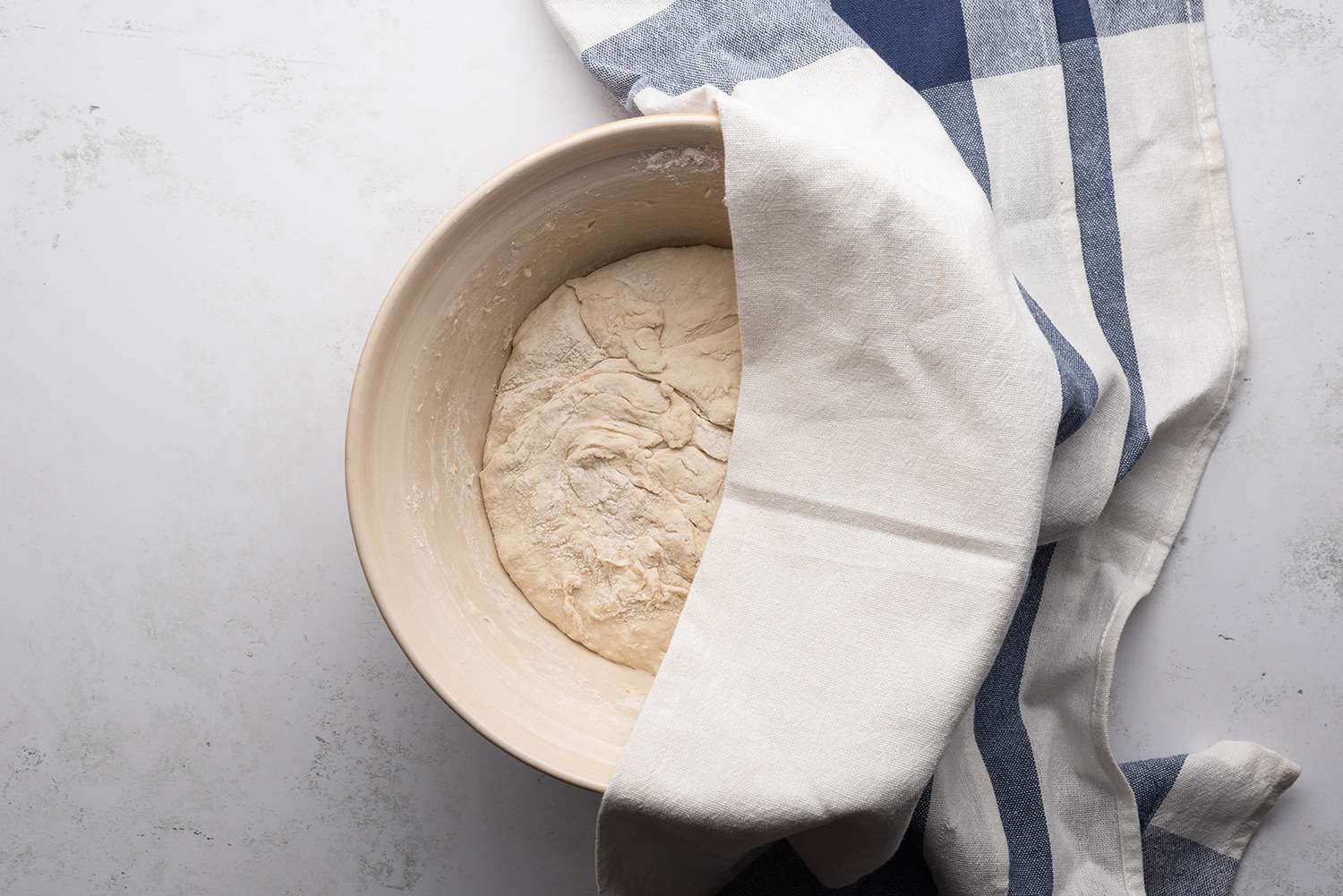 Water, flour, and active starter mixture in a bowl, covered with a towel