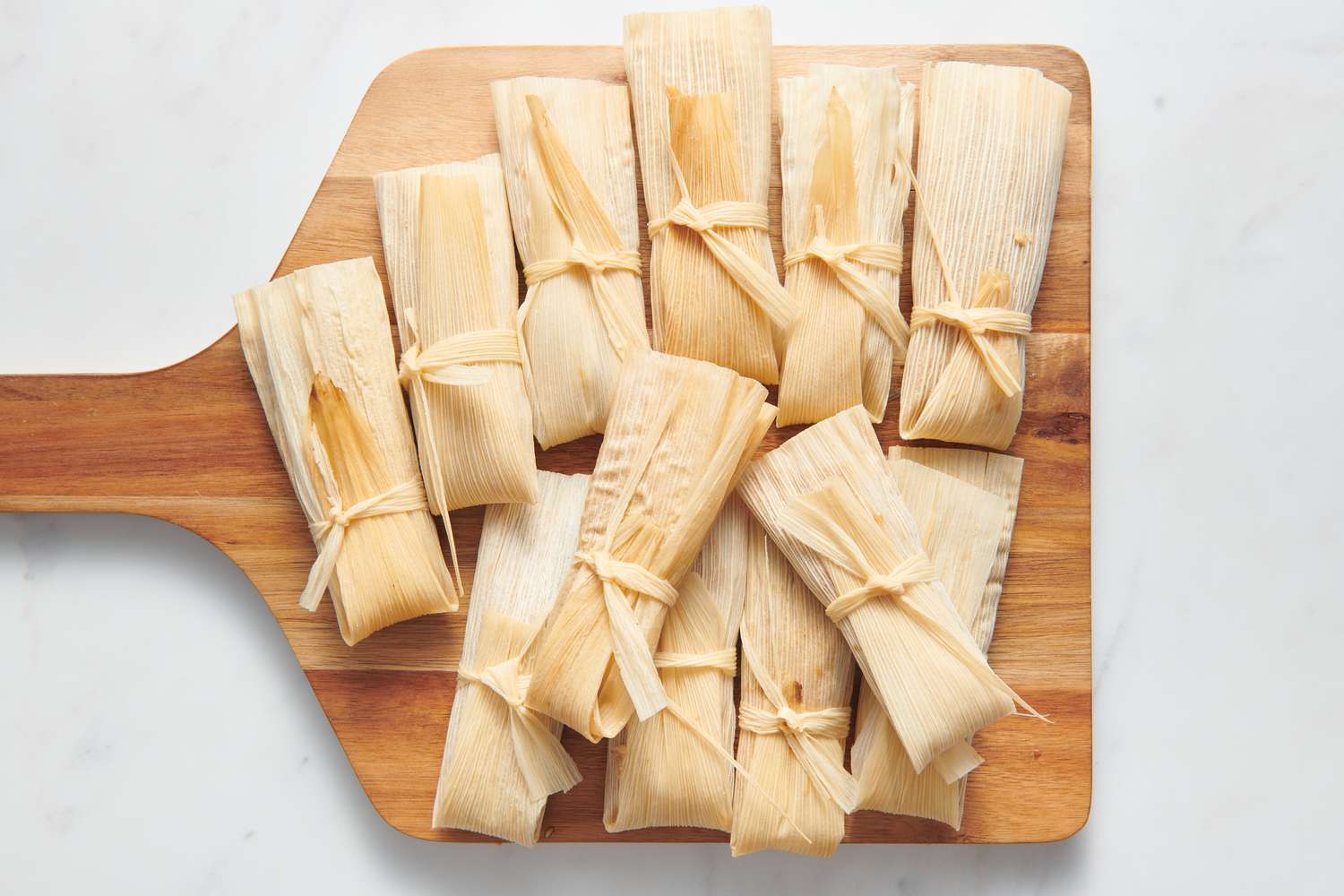 A cutting board with 12 sealed and tied pecan pie tamales