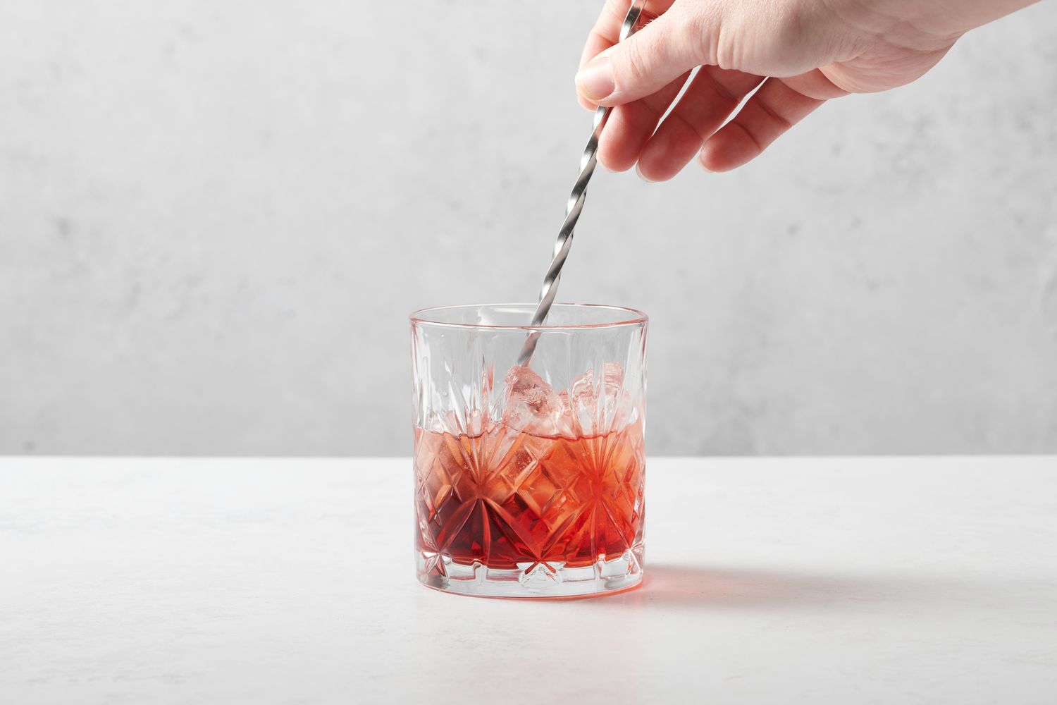 A hand stirring sparkling wine into a rocks glass with Campari and vermouth