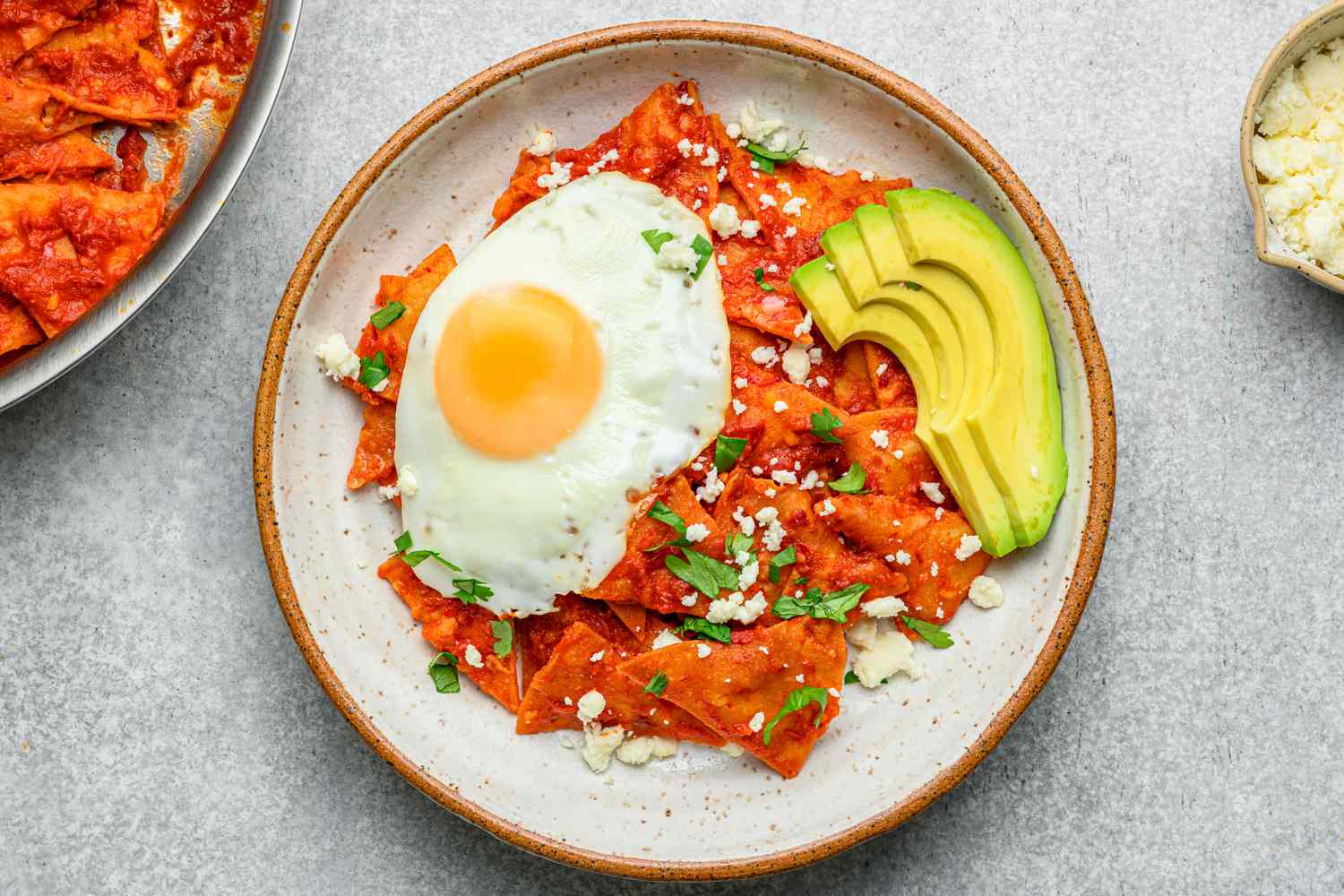 A plate of chilaquiles topped with a friend egg, cilantro, queso fresco, and sliced avocado