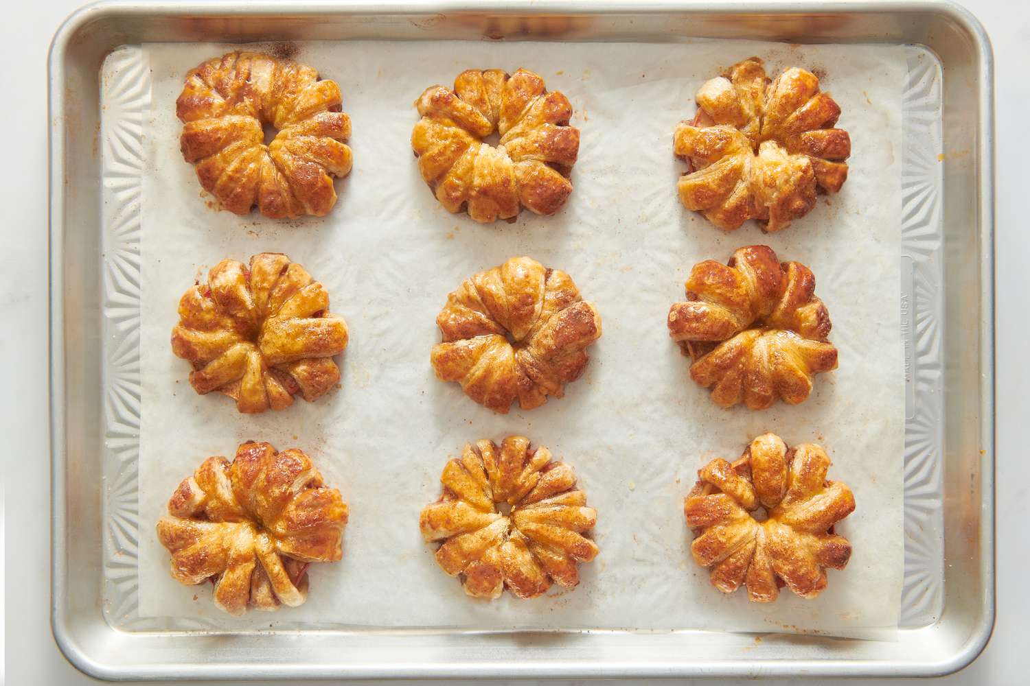 A parchment paper lined baking sheet with baked apple puff pastry doughnuts