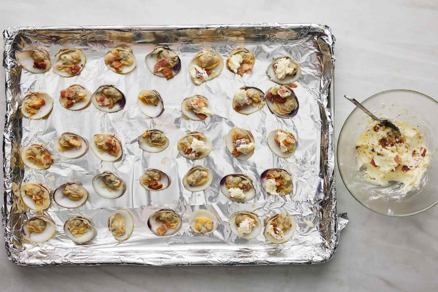 prepared clams on foil lined baking sheet with dollops of the compound butter