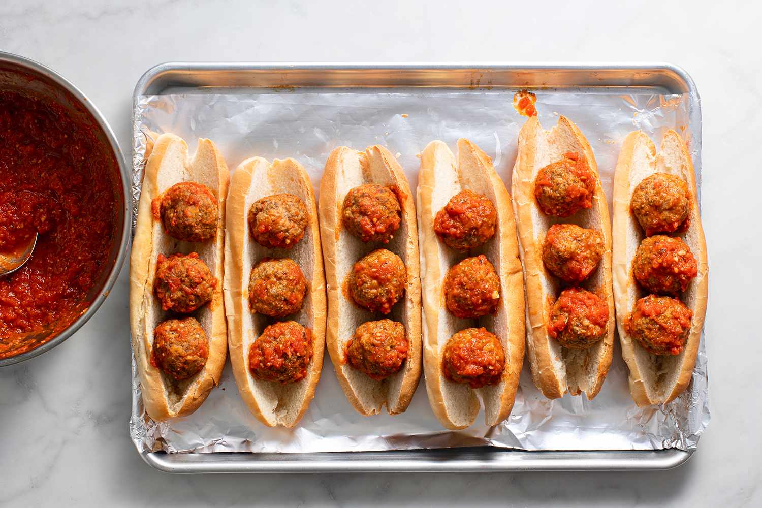 A foil-lined baking sheet with sub rolls filled with meatballs