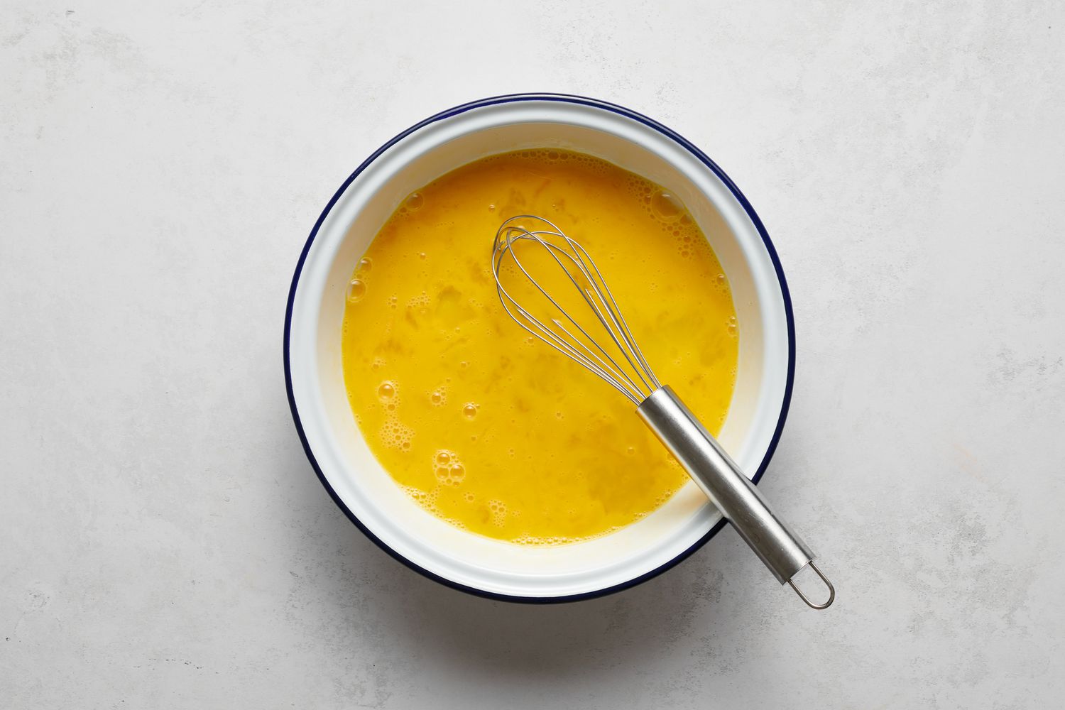 A shallow bowl of beaten eggs with a whisk