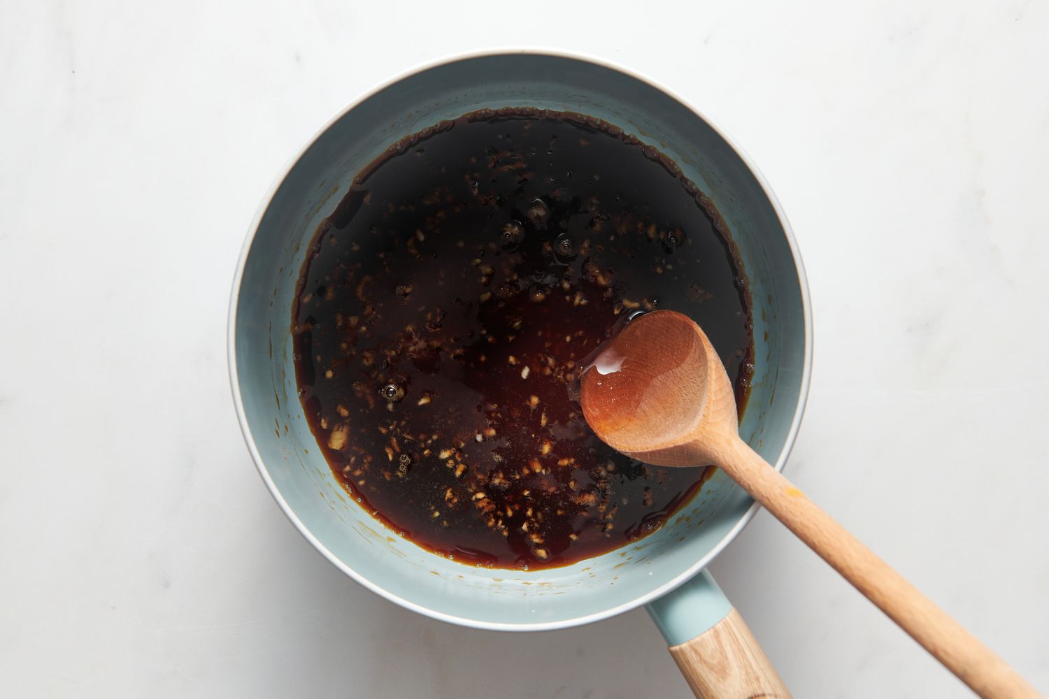 A small pan with soy sauce, honey, garlic, and rice vinegar bring stirred with a wooden spoon