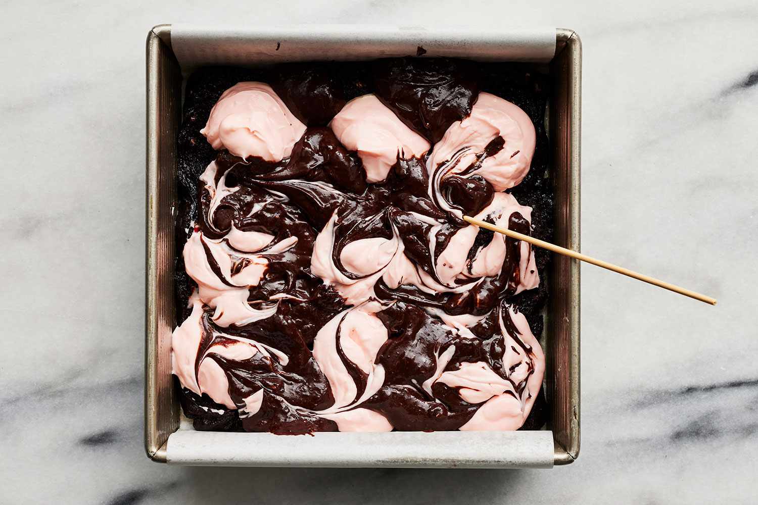 remaining brownie batter being swirled with peppermint cream using a wooden skewer