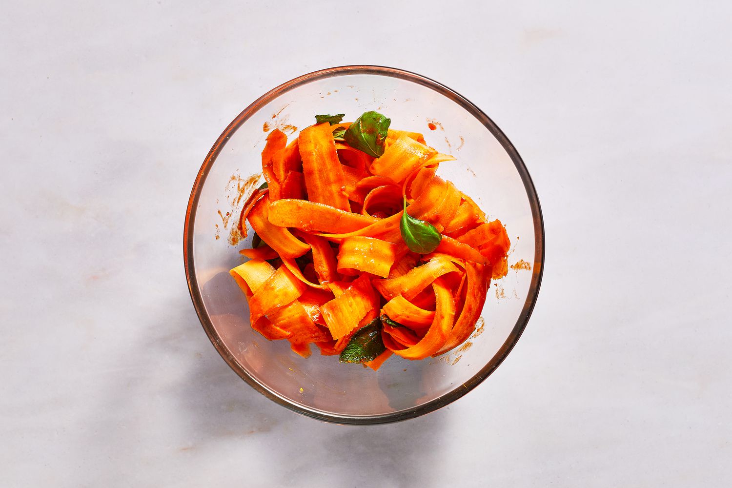 A bowl of shaved carrot ribbons, mint leaves, and basil leaves tossed with gochujang dressing