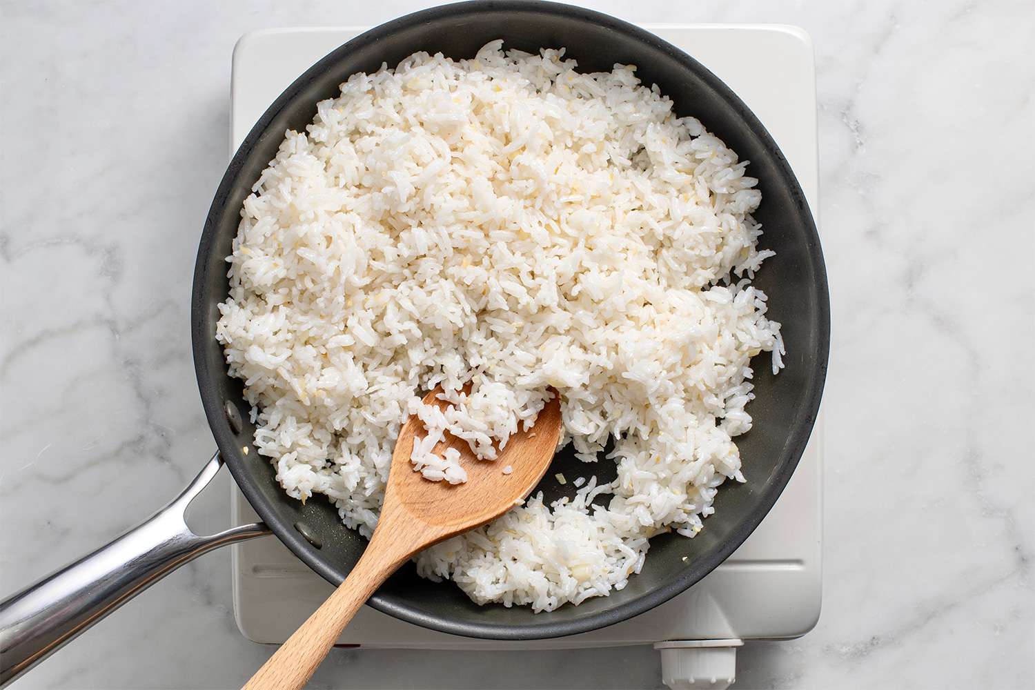 Rice in a skillet on a burner with a wooden spoon 