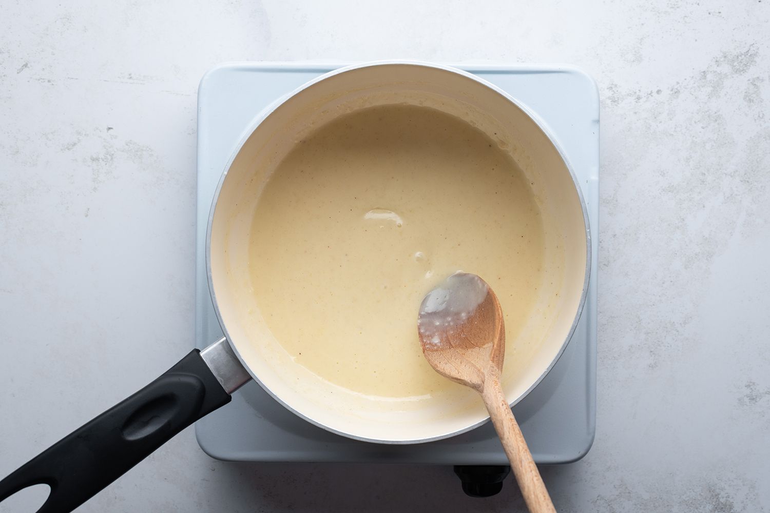 BÃ©chamel sauce sauce in a saucepan with a wooden spoon, on a burner 