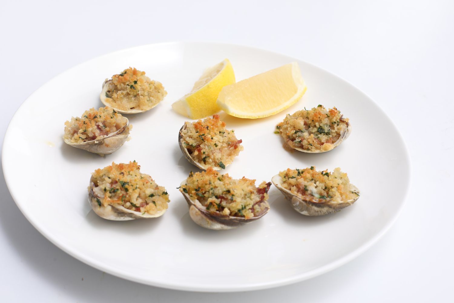 Clams on the half shell topped with a browned breadcrumb mixture and served with two lemon wedges on a white plate