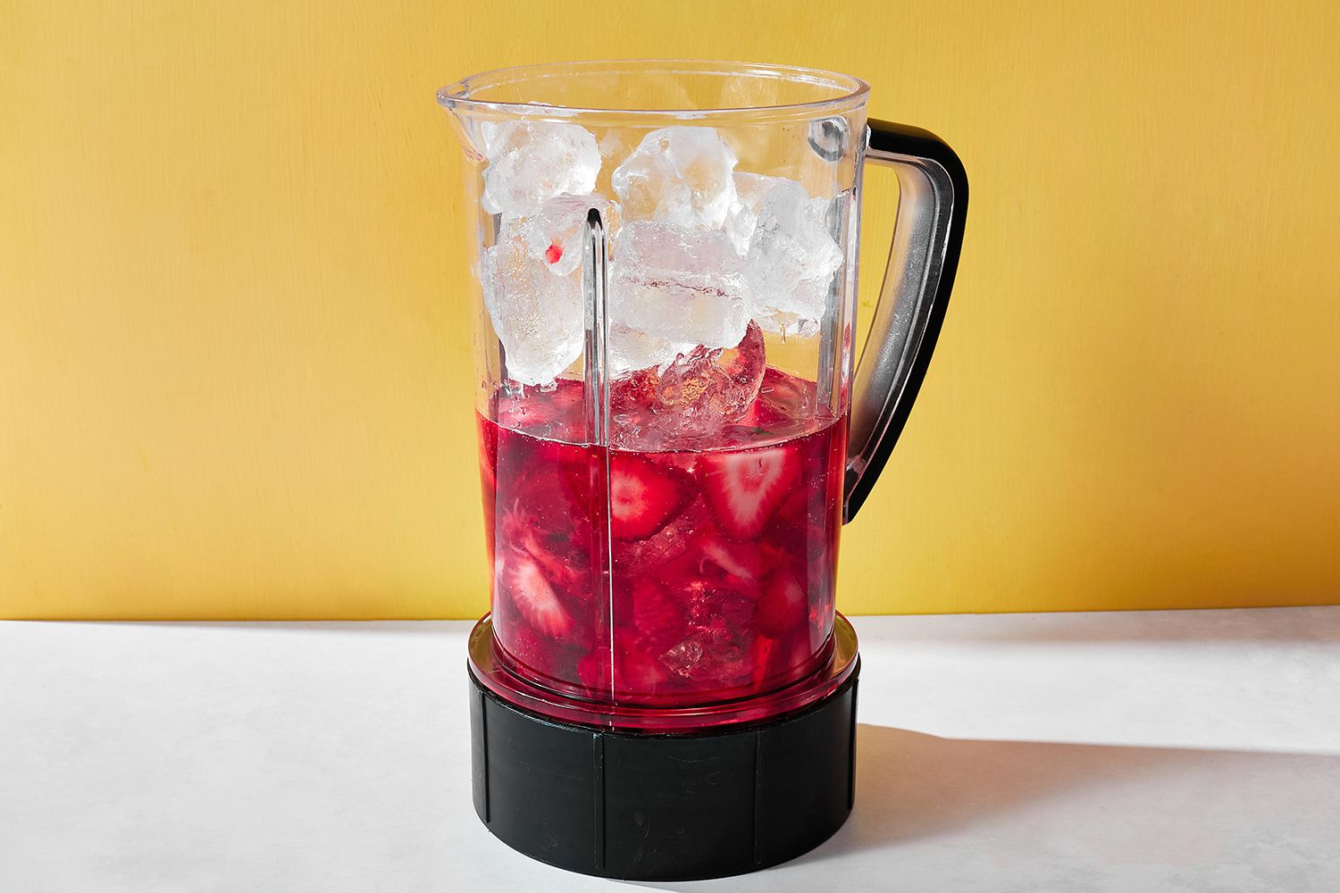 A blender filled with wine, strawberries, ice cubes, sugar, and lemon juice