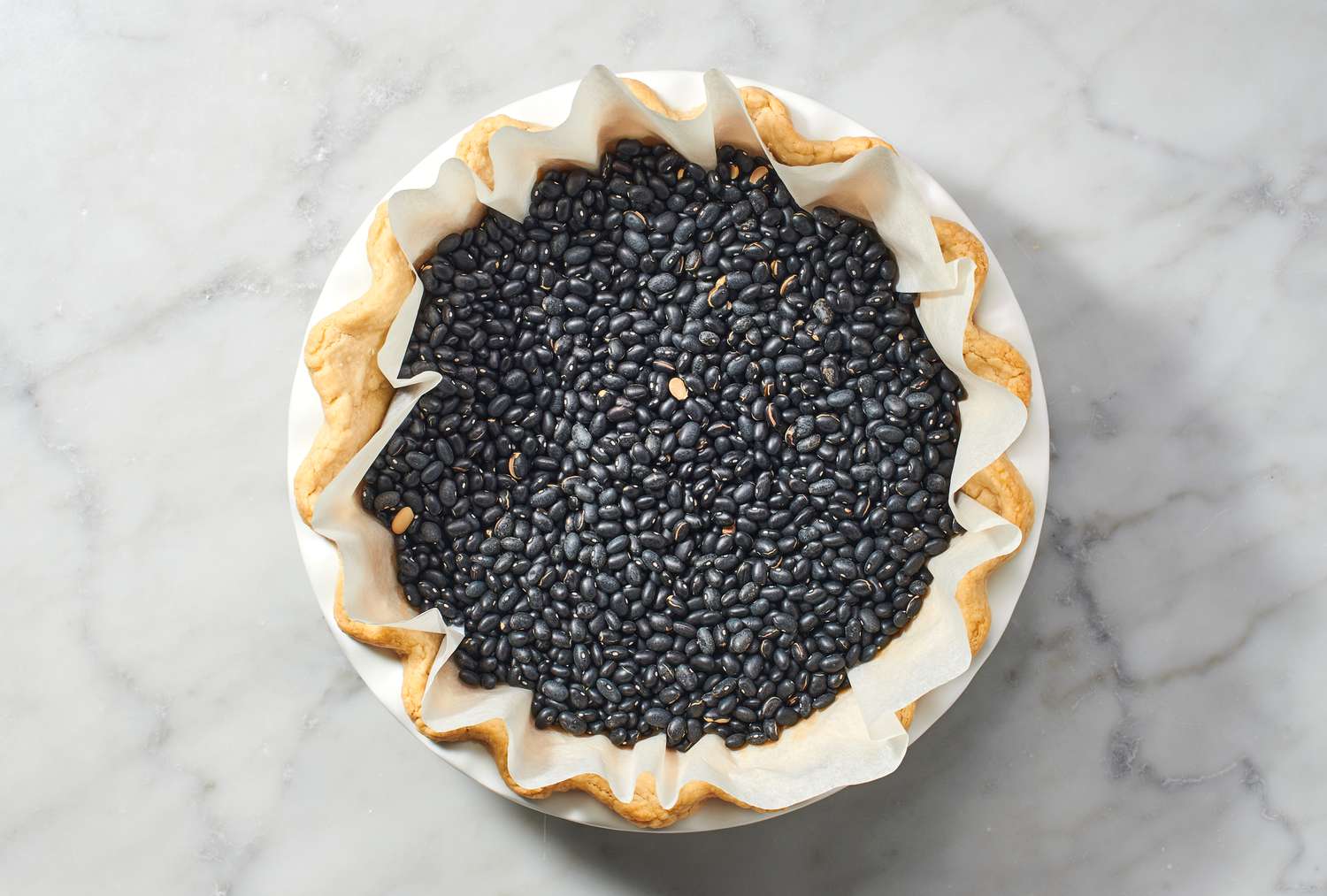 A pie crust in a pie plate lined with parchment paper and black beans
