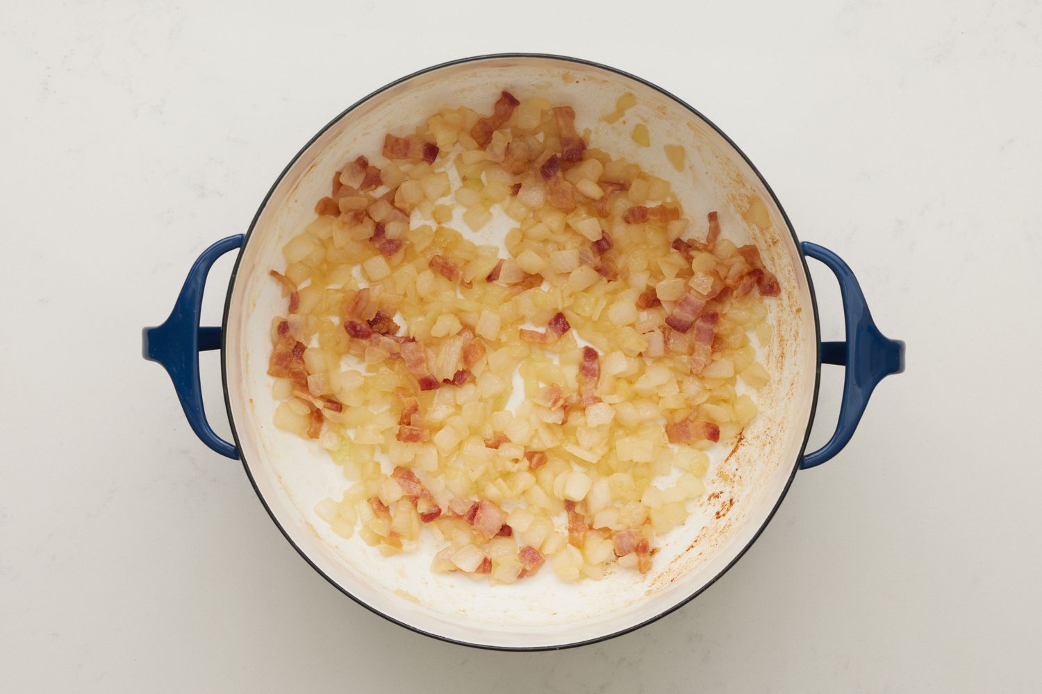 A dutch oven with chopped bacon, diced onions, butter, and flour