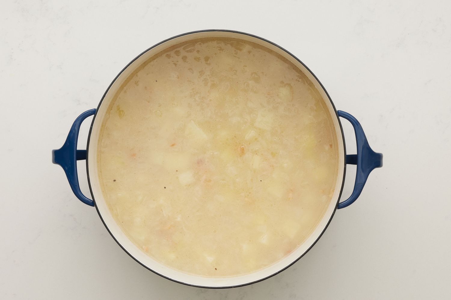 A dutch oven with water, clam juice, and chopped potatoes added to the onion-bacon mixture