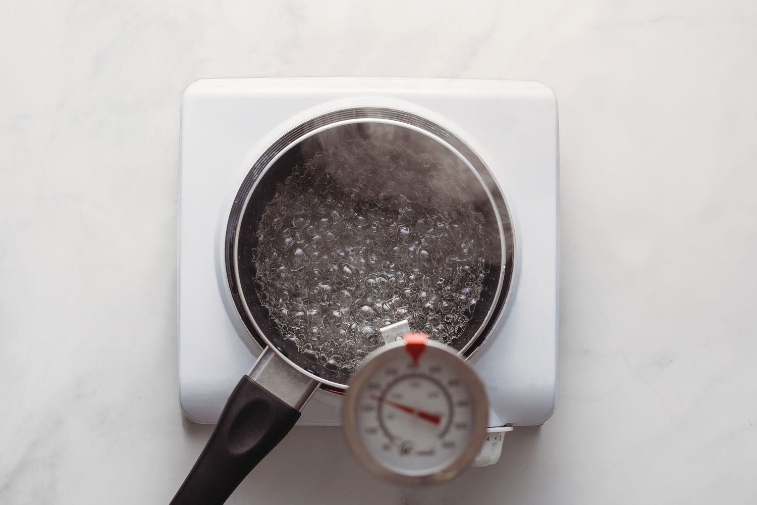Candy thermometer inserted into boiling syrup in the saucepan