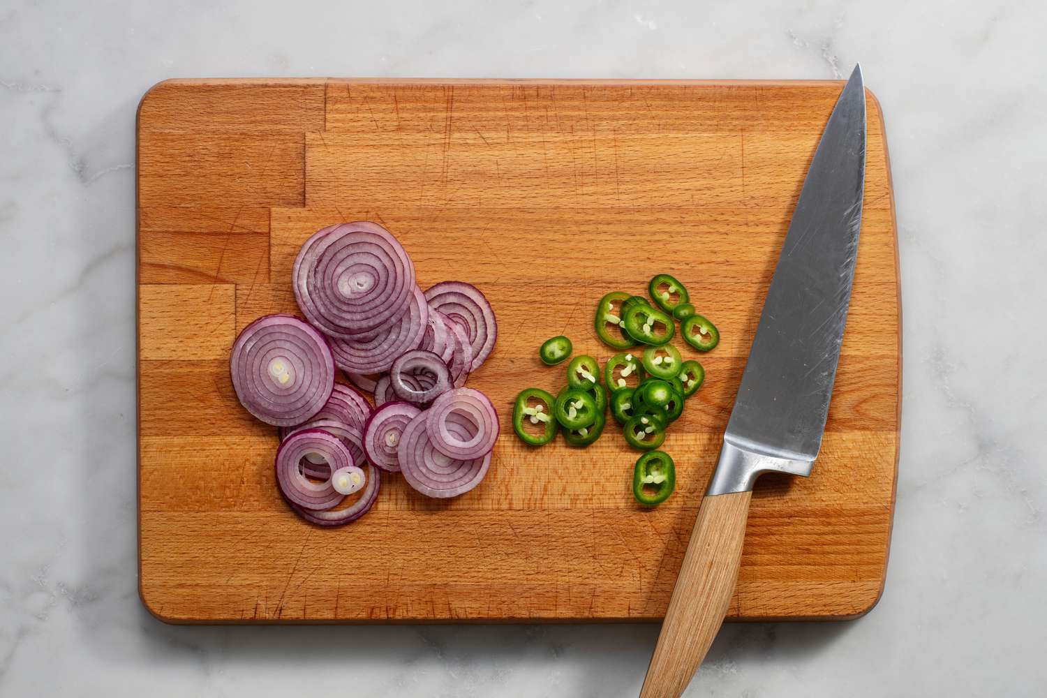 Thinly sliced red onion and jalapenos on a cutting board