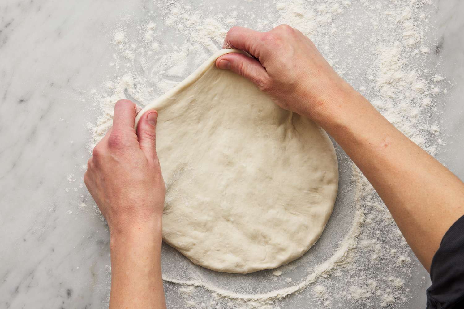 calzone dough being stretched by hand on a floured work surface into a circle