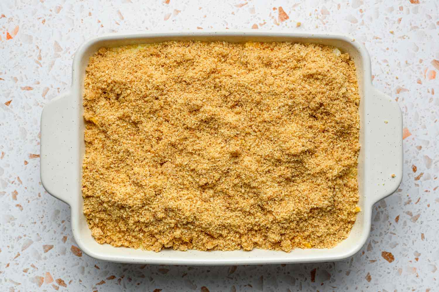 An unbaked yellow squash casserole in a baking dish, topped with breadcrumbs