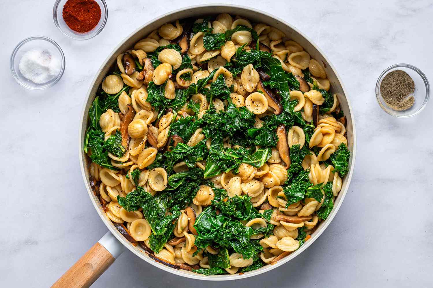 A skillet of pasta, greens, and mushrooms mixed together with smoked paprika, salt, and pepper
