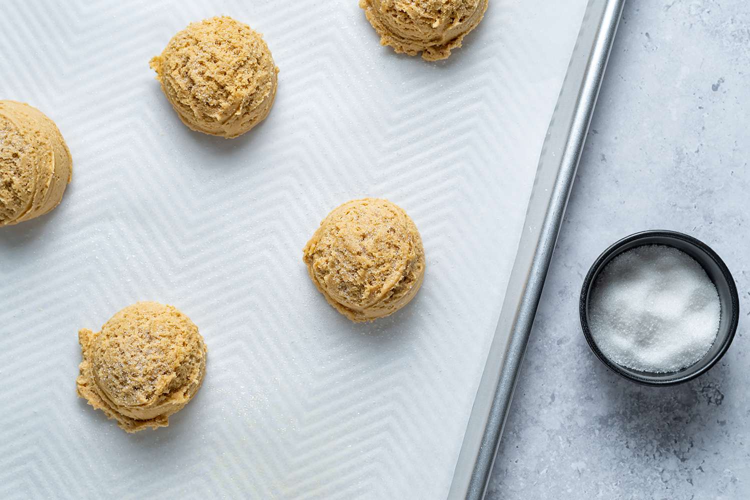 Cookie dough scoops on a lined baking sheet, and granulated sugar in a bowl 